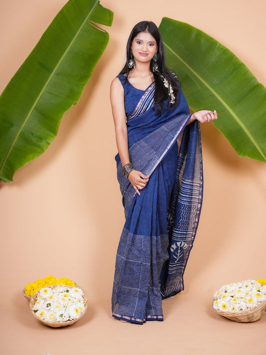 Woman in a blue saree standing between large green leaves on a beige background