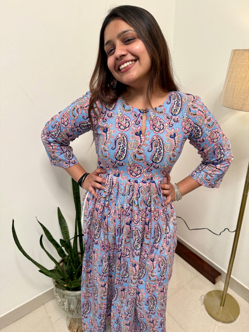A woman smiling and posing in a traditional Alizeh kameez with handcrafted prints, standing indoors.